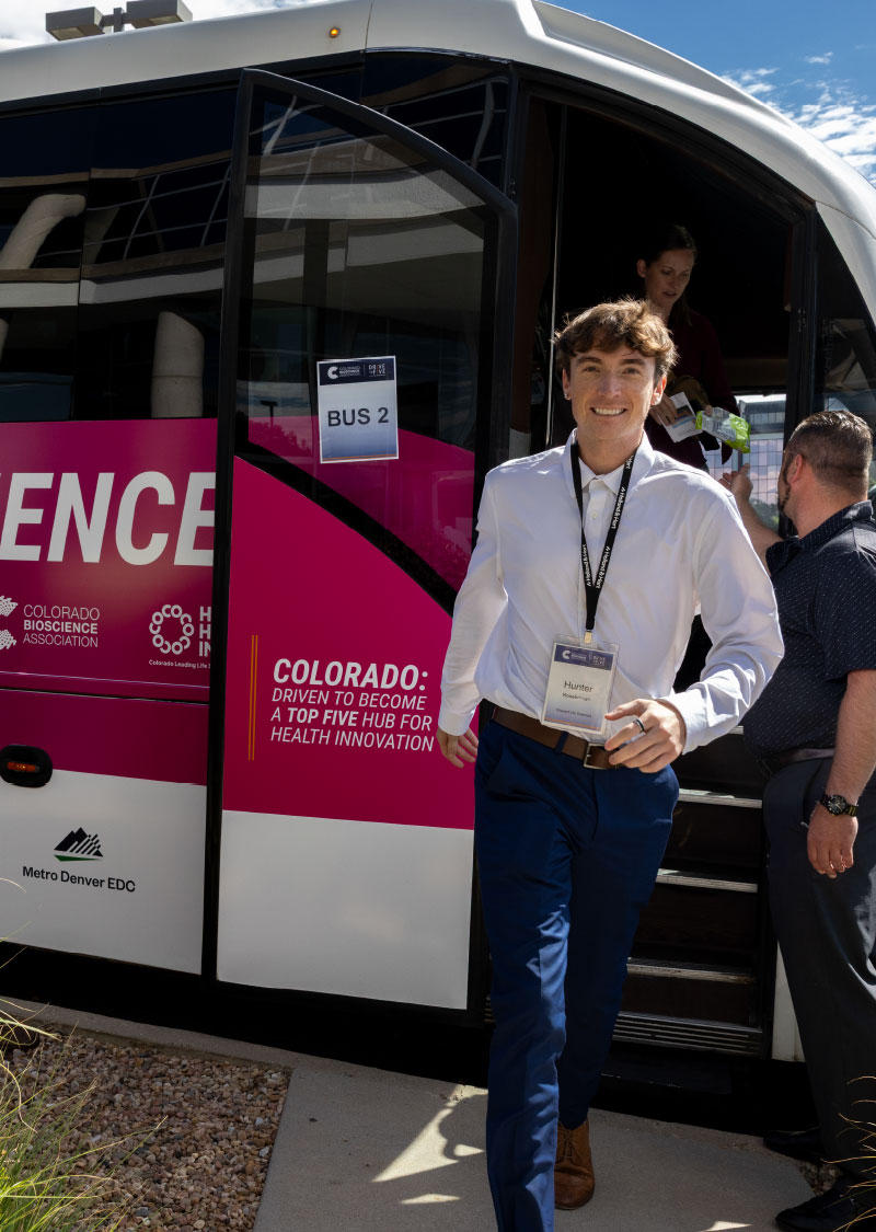 Young, smiling man coming off of the Colorado Life Sciences Innovation Tour bus